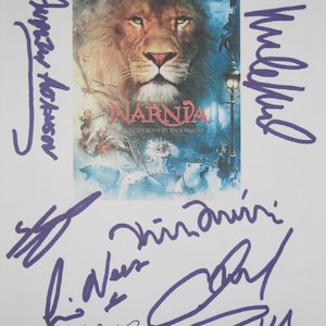 May include: A movie poster for "The Chronicles of Narnia: The Lion, the Witch, and the Wardrobe" featuring a lion's face. The poster is signed in purple ink by several people. The title is in a stylized font.