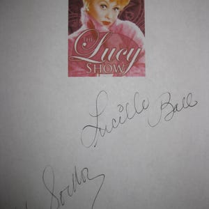 May include: A printed image of Lucille Ball from "The Lucy Show" with her signature and another signature below it. The image of Lucille Ball shows her with blonde hair and wearing a pink outfit. The show's logo is in pink and white.