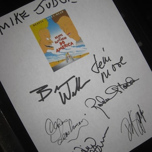 May include: A white sheet with the words "MIKE JUDGE" written in black marker at the top. A small Beavis and Butt-Head movie poster is affixed to the sheet, surrounded by multiple signatures.