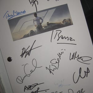 May include: A white sheet of paper with multiple signatures in black ink and a small image of a person in a racing suit. The image is from "F1 The Movie". The signatures are in various styles and sizes.