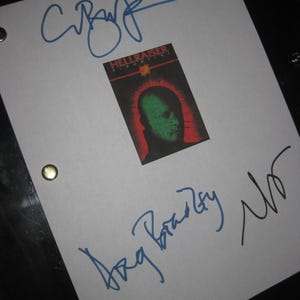 Könnte beinhalten: Ein weißes Blatt Papier mit blauen Tintenunterschriften und einem kleinen Hellraiser-Filmplakat. Das Plakat zeigt eine grüngesichtige Figur mit rotem Hintergrund. Das Papier hat zwei Messingösen.