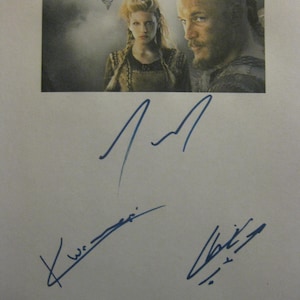 Puede incluir: Imagen impresa con personajes de la serie de televisión "Vikings" y el logotipo de la serie. Debajo, varias firmas en tinta azul, junto con las palabras "Best wishes" y un nombre.
