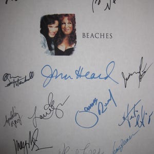 May include: A page featuring multiple signatures in black and blue ink. The word "BEACHES" is printed below a small image of two women. The signatures are of varying sizes and styles, with some overlapping.