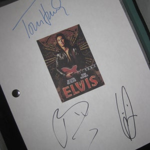 May include: A white sheet of paper with the title "ELVIS" and signatures in blue and black ink. The image on the paper features Austin Butler holding a red guitar. The signatures appear to be from Tom Hanks and others.