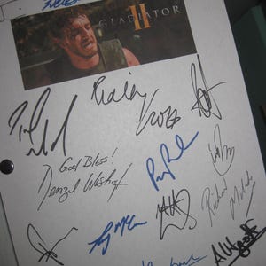 May include: A white sheet of paper with multiple signatures from actors and actresses. The signatures include Denzel Washington, Russell Crowe, and others. The paper has a small photo of Russell Crowe in the movie Gladiator II.