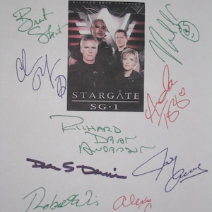 Może przedstawiać: Promocyjny obraz Stargate SG-1 z obsadą, pokryty podpisami w różnych kolorach. Obraz zawiera tytuł serialu i nazwiska aktorów. Podpisy są w kolorze zielonym, fioletowym i czerwonym.