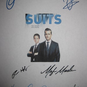 May include: A promotional image for the TV show "Suits" featuring two actors in suits. The title "Suits" is in blue block letters. The image is surrounded by multiple signatures in blue and black ink.