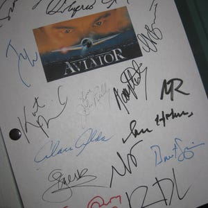 May include: White paper with multiple signatures in black, blue, and red ink. A small image from "The Aviator" movie is in the center. The signatures surround the image and are of varying sizes and styles.