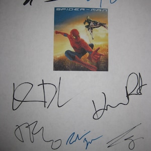 Op de afbeelding: Een wit papier met meerdere handtekeningen in zwarte inkt en een kleine Spider-Man filmposter. De poster toont Spider-Man in een rood-blauw pak, met de woorden "SPIDER-MAN" bovenaan.