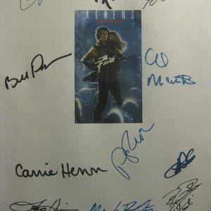 May include: A page featuring the movie poster for "Aliens" with multiple signatures in black and blue ink. The poster shows a person holding another person with a weapon. The name "Carrie Henn" is visible.