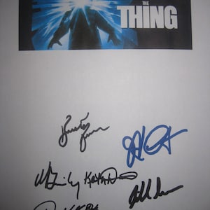 May include: A promotional card for John Carpenter's "The Thing" film, with a blue and white graphic of a figure with a bright light emanating from its head. The card is signed by multiple people.
