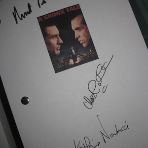 May include: A white sheet of paper with the movie poster "A Bronx Tale" affixed to it. The poster features two men's faces. Several signatures are written in black ink on the paper.