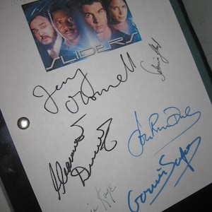 Op de afbeelding: Een wit papier met een afgedrukte afbeelding van de tv-serie "Sliders" en meerdere handtekeningen in zwarte en blauwe inkt. De afbeelding toont vier personen. De handtekeningen zijn in verschillende stijlen.