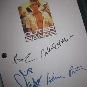 May include: A white sheet of paper with a printed image of the "Outer Banks" show and several signatures in black and blue ink. The image features a man in a button-down shirt. The text "Outer Banks" is printed in a bold, white font.