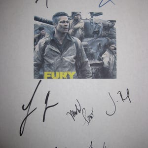 Può includere: Un poster del film "Fury" con Brad Pitt, circondato da firme a inchiostro nero. Il poster mostra soldati e un carro armato, con la parola "FURY" in giallo.