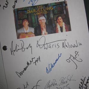 May include: A white sheet with multiple signatures and a small image from "The Darjeeling Limited" film. The image features three men. The signatures are in black and blue ink.