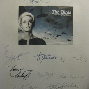 May include: A black and white image of a movie poster for "The Birds" featuring Tippi Hedren. The poster is signed by multiple people. The title is in a bold, white font, with the actress's name below.