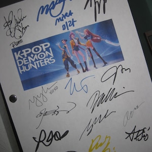 Op de afbeelding: Wit papier met meerdere handtekeningen in blauwe, zwarte en gele inkt. Een centrale afbeelding toont drie geanimeerde figuren uit "K-Pop Demon Hunters". De tekst "K-Pop Demon Hunters" is ook zichtbaar.