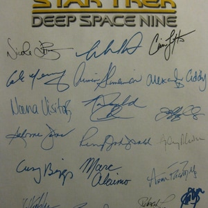 Op de afbeelding: Een wit vel papier met de woorden "STAR TREK DEEP SPACE NINE" in gele en zwarte letters. Het papier is gesigneerd door verschillende mensen, waaronder Ray Boje, Cole for an, Dana Visito, Jamie Dietcher en Cecily Adan.