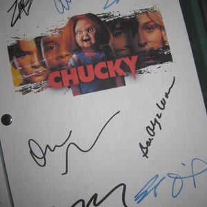 Peut inclure: Une feuille de papier blanche avec le mot "CHUCKY" en rouge et une image de la poupée Chucky. Le papier est couvert de signatures à l'encre bleue et noire.
