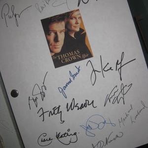 May include: A white sheet with multiple signatures in black and blue ink. A small image from "The Thomas Crown Affair" movie is in the center. The sheet is held together with two black metal fasteners.