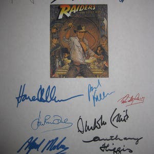 Könnte beinhalten: Ein Druck des Filmplakats für "Jäger des verlorenen Schatzes" mit Harrison Ford, umgeben von mehreren Unterschriften in blauer und schwarzer Tinte. Die Plakatkunst zeigt Indiana Jones mit einer Peitsche.