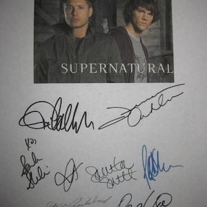 Könnte beinhalten: Ein gedrucktes Bild mit zwei Männern aus der Fernsehserie "Supernatural". Der Titel "Supernatural" ist in weißen Blockbuchstaben gedruckt. Darunter befinden sich mehrere Unterschriften in schwarzer und blauer Tinte.