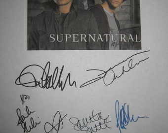 May include: A printed image featuring two men from the television show "Supernatural." The title "Supernatural" is printed in white block letters. Below the image are several signatures in black and blue ink.