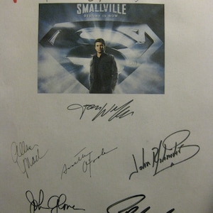 May include: A white background with a black and white image of a man in front of a Superman logo. The image is from the TV show Smallville. The text "Destiny is Now" is below the logo. The image is surrounded by several autographs in black ink.