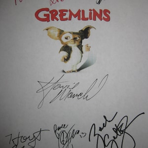 Puede incluir: Una hoja de papel blanca con firmas en negro y rojo. Las firmas incluyen "Phoebe Cates", "Steven Spielberg", "Hoyt Axton", "Corey Feldman" y "Zach Galifianakis". El papel también tiene el título "Gremlins" en letras rojas y una ilustración en blanco y negro de Gizmo, la linda criatura peluda de la película.
