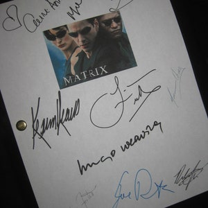 May include: A white sheet of paper with multiple signatures from the cast and crew of the movie "The Matrix". The signatures include: "Carrie-Anne Moss", "Keanu Reeves", "Hugo Weaving", "Joe Pantoliano", "Lana Wachowski", and "Lilly Wachowski".
