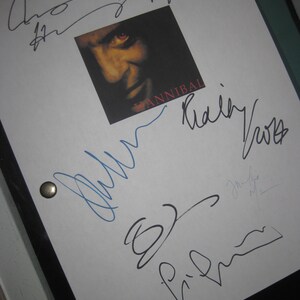 May include: A white sheet with multiple signatures in black and blue ink. A small square image of a man's face with red eyes and the word "HANNIBAL" is in the center. Two silver metal fasteners are visible.