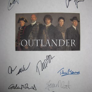 May include: A signed Outlander cast photo featuring the main characters from the TV show. The photo is signed by Caitriona Balfe, Sam Heughan, Tobias Menzies, Graham McTavish,  and  the show's creator,  Ronald D. Moore.
