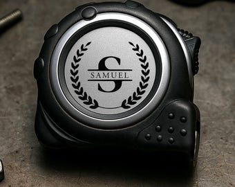 May include: A black and silver tape measure featuring the name "SAMUEL" and the letter "S" within a laurel wreath. The image also shows a wrench, screwdrivers, screws, and nuts, all arranged on a metallic surface.