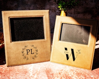 May include: Two tan leather picture frames with a stitched border. The frame on the left has the initials "PL" in a wreath design. The frame on the right has the initial "W" with a small flower design.