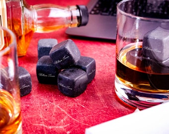 May include: A set of six black whiskey stones with the text "William Turner" engraved on each stone. The stones are in a glass with whiskey and a bottle of whiskey is in the background.