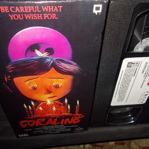 May include: A VHS tape and box set for the animated film "Coraline." The box art features a sad-looking girl with candles and a large button. The text "BE CAREFUL WHAT YOU WISH FOR" is at the top.