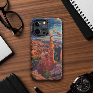 Puede incluir: Una funda para teléfono con una imagen colorida de una alta formación rocosa roja en un paisaje desértico. La funda tiene una protuberancia de cámara negra con tres lentes.