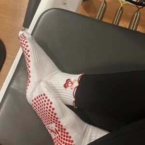 May include: White socks with red dots and a red flower design on the ankle. The socks are worn on a person's feet, with black leggings.