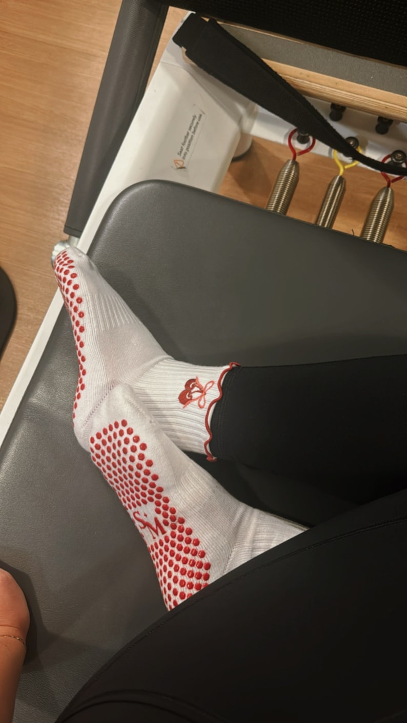 May include: White socks with red dots and a red flower design on the ankle. The socks are worn on a person's feet, with black leggings.
