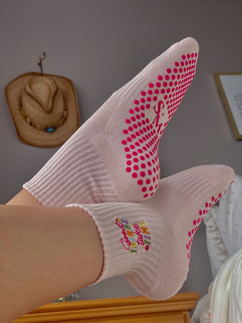 Pu&ograve; includere: Coppia di calzini rosa con pois rosa sul fondo e il testo "Good things take time" ricamato su un calzino.