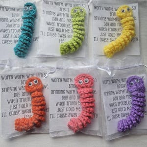 Puede incluir: Seis juguetes de gusano de la preocupación hechos a crochet en diferentes colores, cada uno con una etiqueta que dice "Worry Worm, with yarn so bright, bringing warmth day and night, when troubles come just hold me tight, I'll chase away your fear."