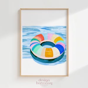 Può includere: Una stampa d'arte incorniciata raffigurante un dipinto di un salvagente da piscina a righe multicolori su acqua blu. Il salvagente presenta segmenti rossi, rosa, gialli, azzurri, verdi e arancioni. Il testo design harmony studio co. è in basso.