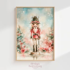 May include: A watercolor-style art print featuring a central nutcracker figure wearing a red uniform and tall hat, flanked by two stylized evergreen trees with red accents, set against a soft, snowy, light blue and peach-toned background.