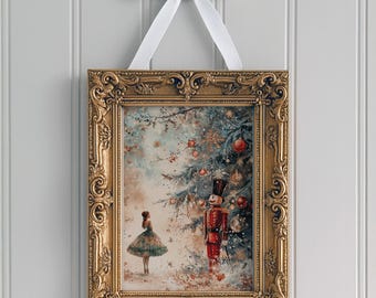 May include: A framed Christmas-themed print with a gold ornate frame, hanging from a white ribbon bow. The artwork depicts a ballerina, a nutcracker, and a decorated Christmas tree with red ornaments. The overall color palette is soft with muted tones.