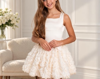 May include: A sleeveless cream-colored dress featuring a smooth, solid bodice with a square neckline and a voluminous, textured skirt composed of layered, ruffled fabric rosettes that create a dense, floral-like appearance throughout the hem.
