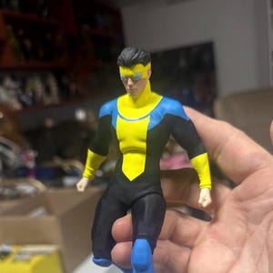 Puede incluir: Figura de acción detallada de un superhéroe en una pose dinámica. La figura está vestida con un traje negro, amarillo y azul, con una máscara amarilla. El diseño de la figura es muy detallado, con un enfoque en el físico y el disfraz del personaje.