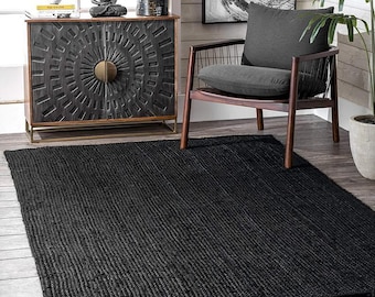 May include: A rectangular black jute rug with a textured, ribbed surface. The rug is placed on a wooden floor, and is part of a home decor setting. The rug is a solid color and appears to be made of natural fibers.