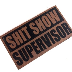 May include: Brown leather patch with black text that reads "Shit Show Supervisor".