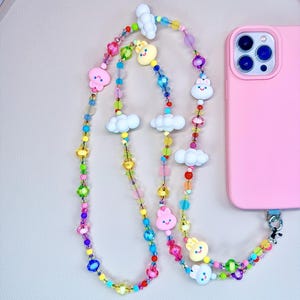 Puede incluir: Un charm de teléfono colorido con una cadena de cuentas de arcoíris y encantadores amuletos de dibujos animados de nubes y conejos.